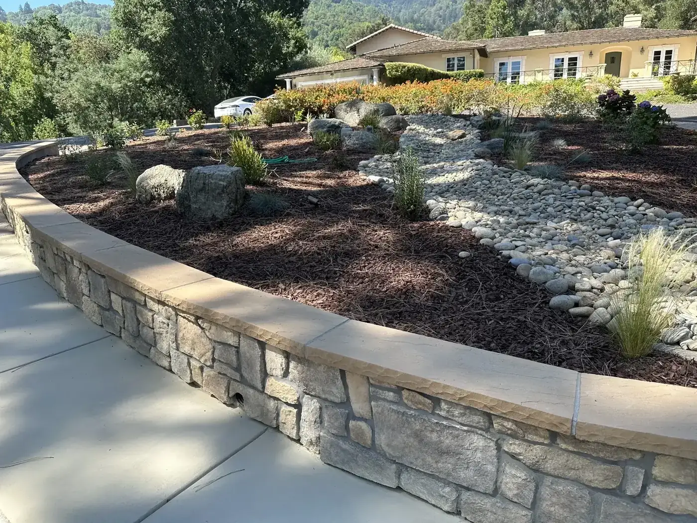 Curved block retaining wall with a dry creek bed and drought-tolerant planting